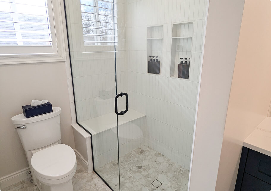Custom bathroom renovation featuring a frameless glass walk-in shower with marble tile flooring, built-in shower niche, and matte black hardware by Odyssey Custom Contracting