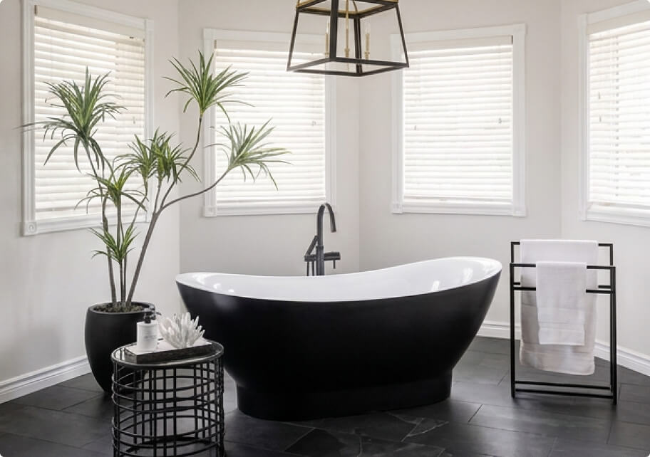 Luxury bathroom renovation featuring a black and white freestanding soaking tub, dark slate tile flooring, modern black fixtures, and gold cage pendant light by Odyssey Custom Contracting