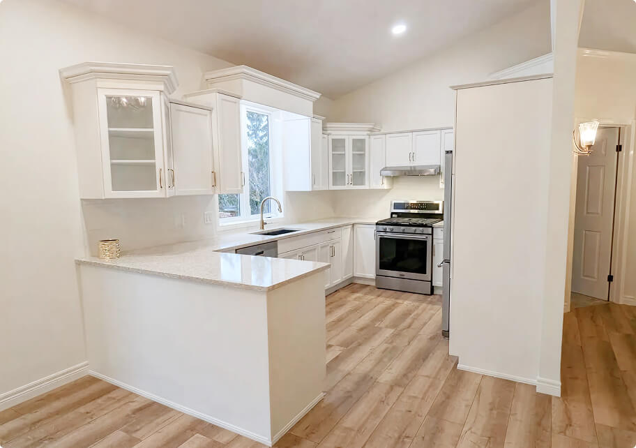 Custom kitchen renovation featuring white shaker cabinets, quartz island countertop, stainless steel appliances, and hardwood flooring by Odyssey Custom Contracting