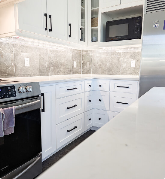 Kitchen renovation featuring white shaker cabinets with black hardware, grey marble tile backsplash, built-in microwave, and black appliances by Odyssey Custom Contracting