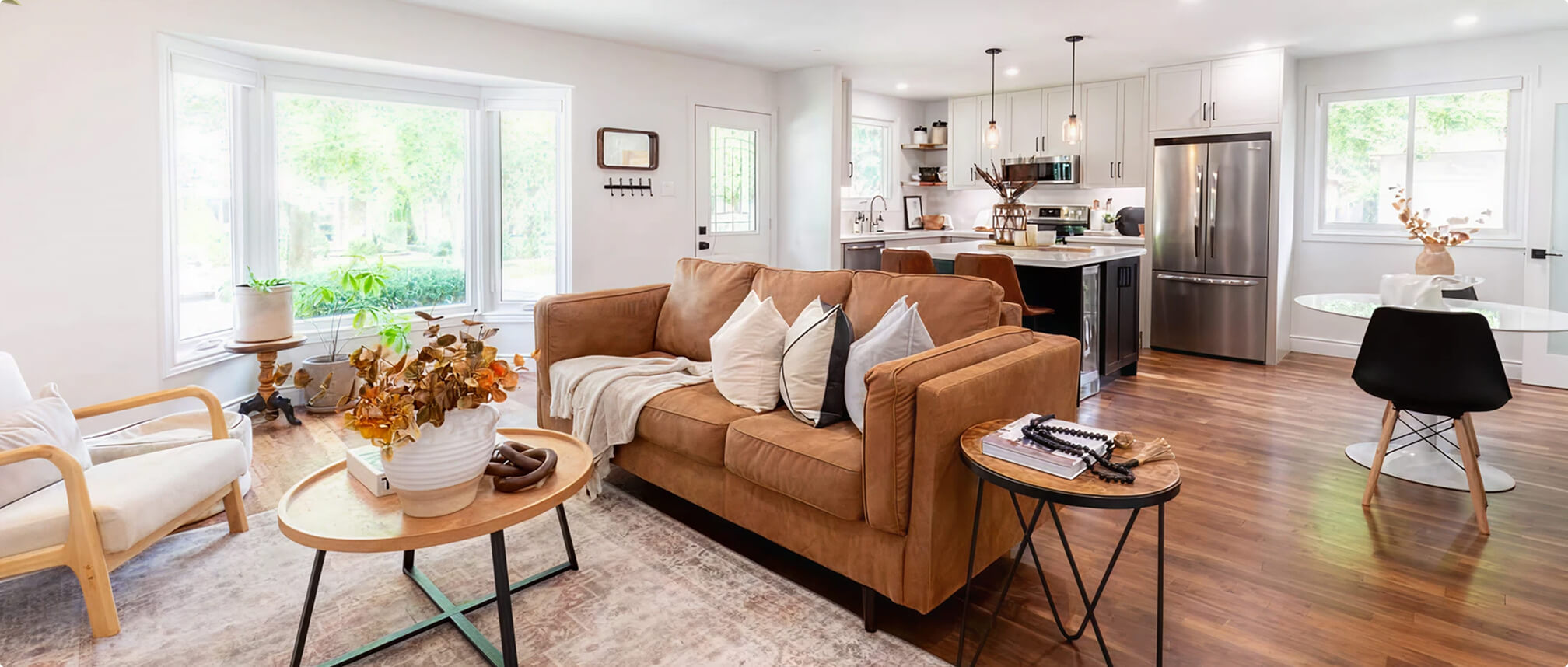 Custom home renovation project showcasing an open-concept living room with caramel sofa and modern coffee tables flowing into an updated kitchen with dark island by Odyssey Custom Contracting